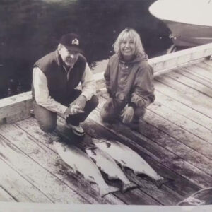 black and white photo of a man and a woman smiling next to three fish on the dock