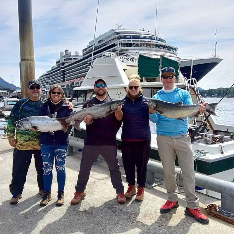 friends posing with three big fish they caught in front of a huge boat